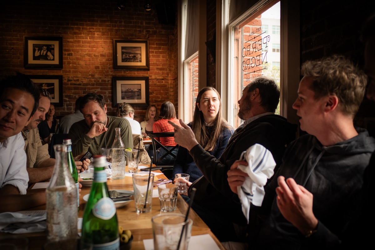 Members deep in conversation down a long table at Perro Negro