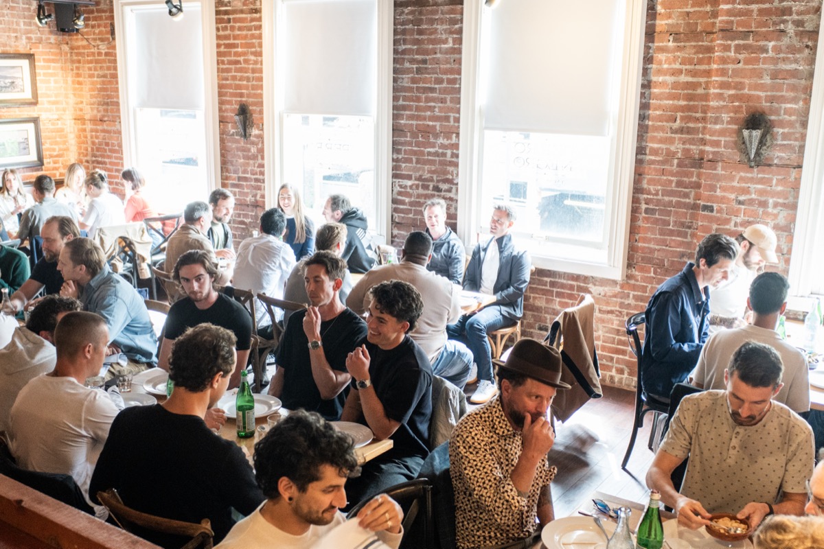 A packed restaurant with exposed brick, every table full of founders mid-conversation