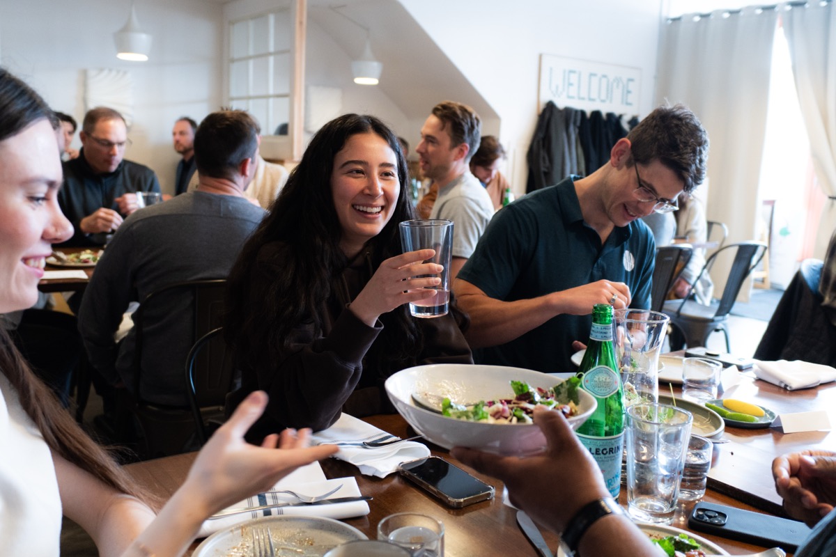 A member raising a glass of water mid-toast at a crowded lunch table